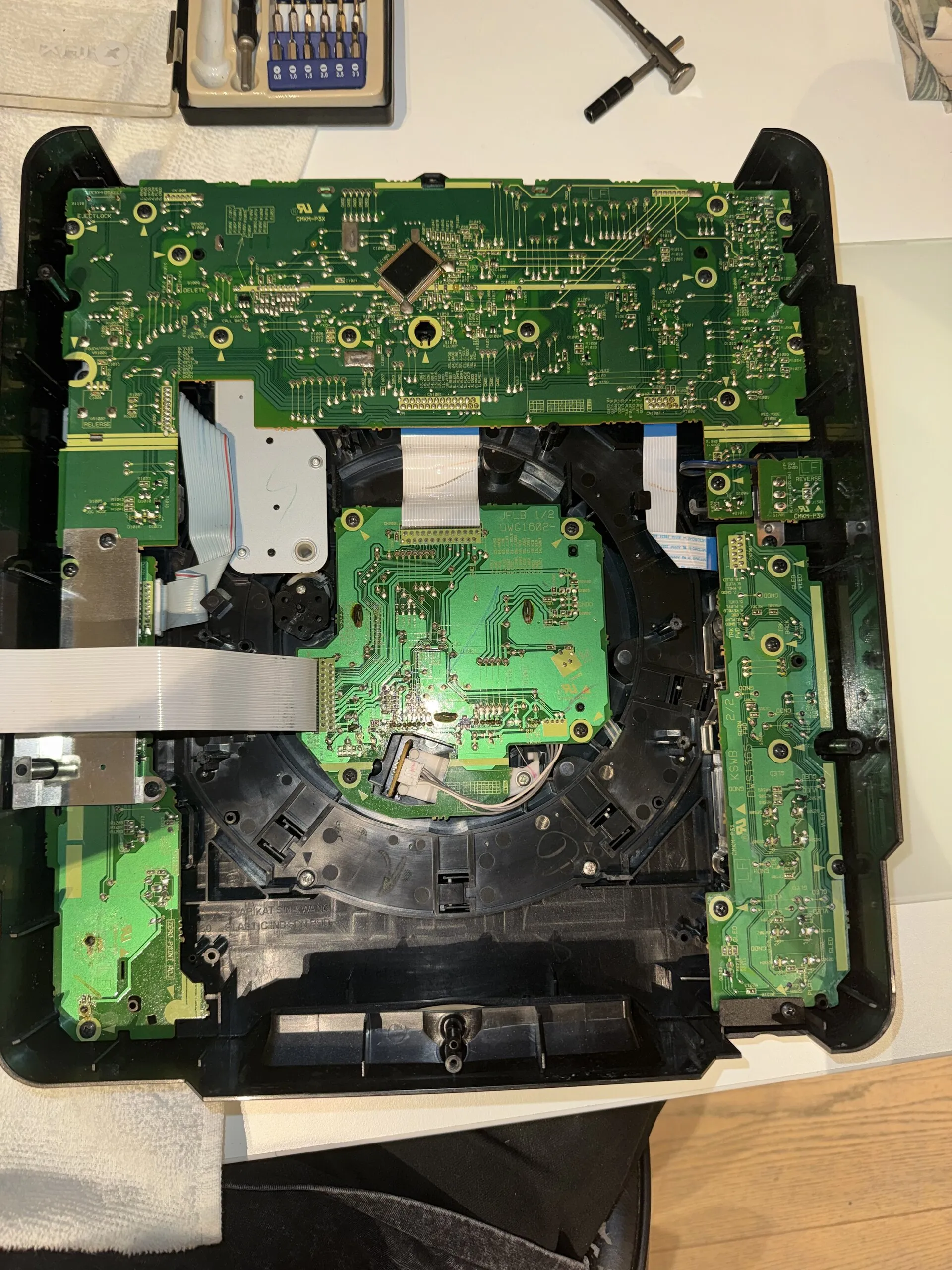 The inside of a CDJ's top panel, face down: green circuit boards for the buttons and the jog, ribbon cables, and the jog mechanism in the middle.
