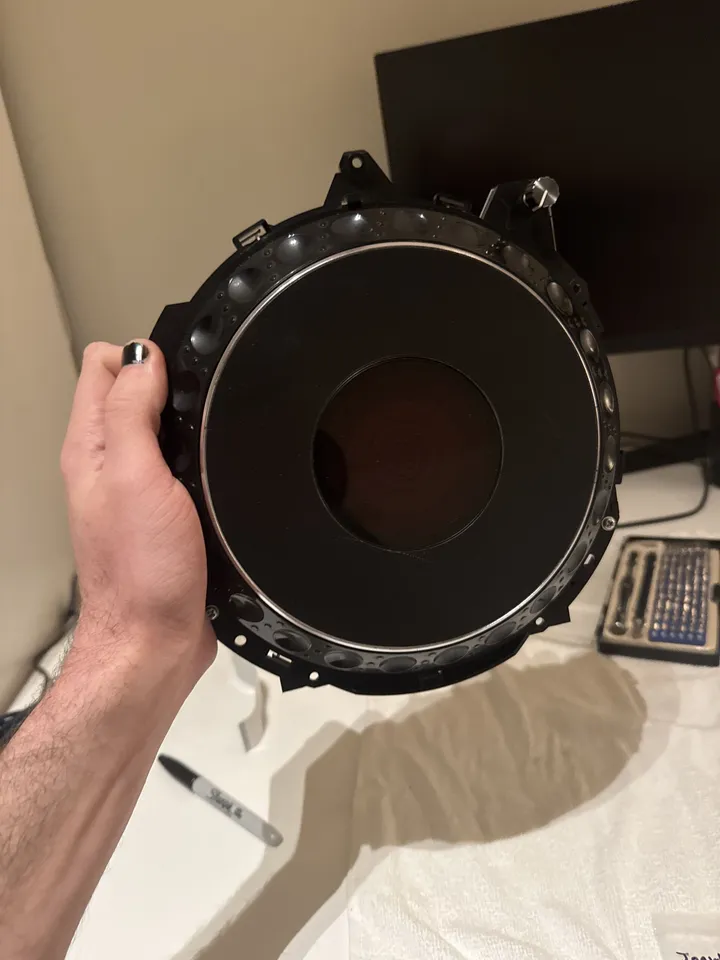 A hand holds the round jog wheel assembly: a black platter with a chrome rim and a dark window at its centre.