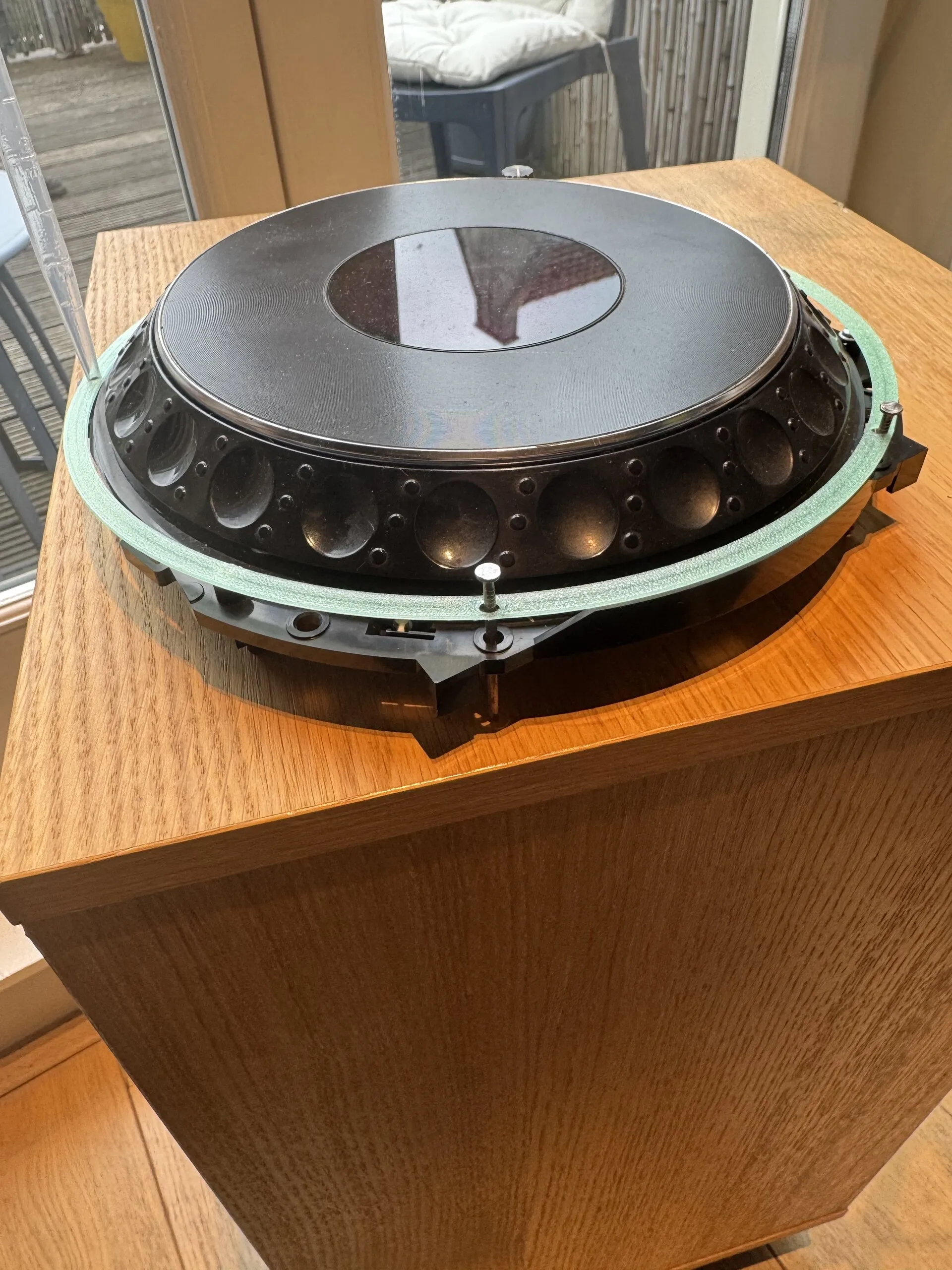 The CDJ-1000MK3 jog assembly on a wooden cabinet, inside a thin translucent green printed ring held by steel pins.