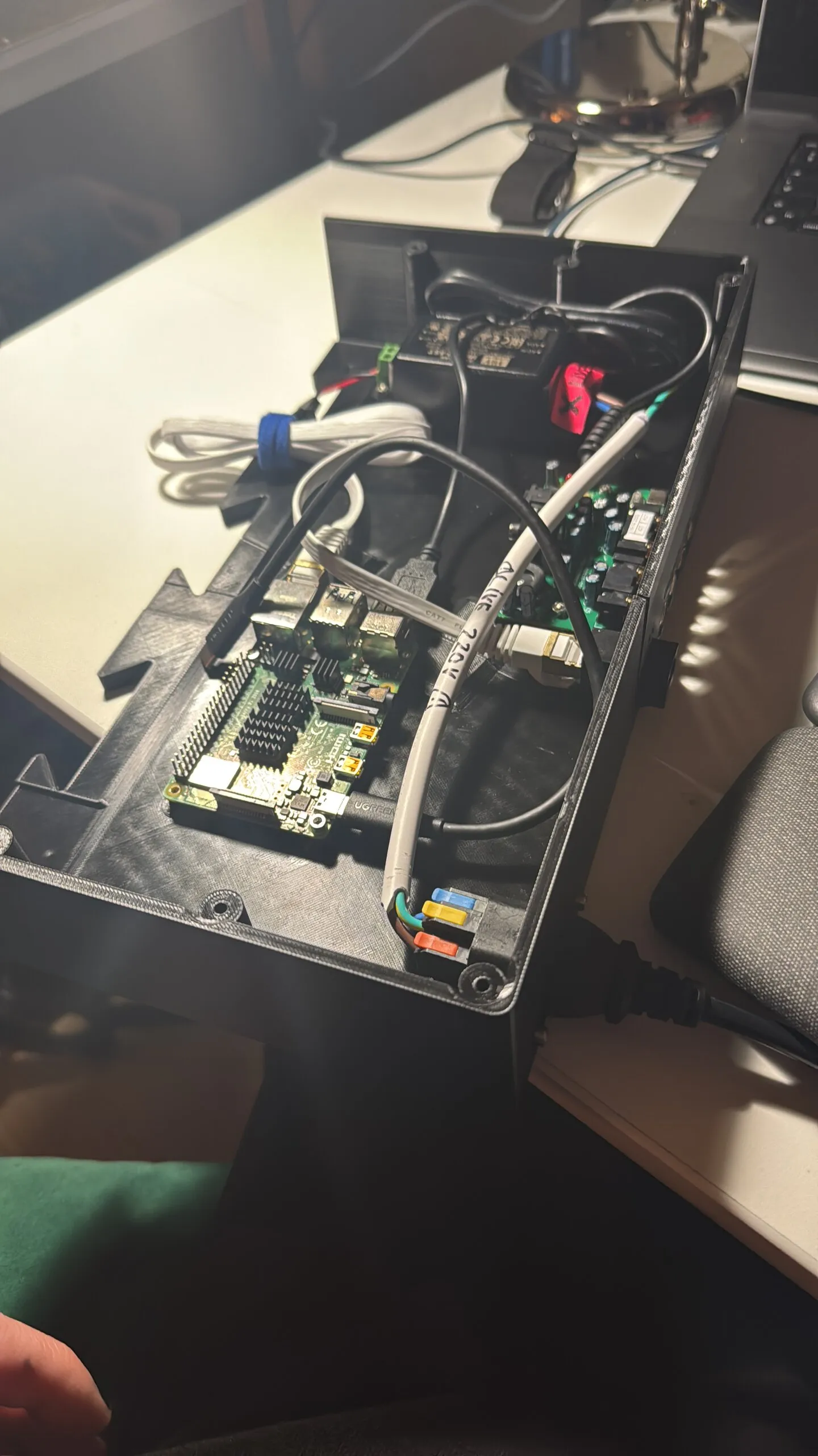 An open black printed tray holding a Raspberry Pi 4 with heatsinks, a green audio board with RCA jacks, a power supply, lever connectors and a grey mains cable.