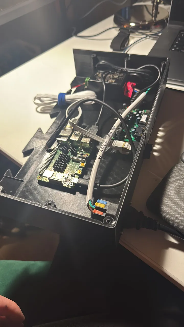 An open black printed tray holding a Raspberry Pi 4 with heatsinks, a green audio board with RCA jacks, a power supply, lever connectors and a grey mains cable.
