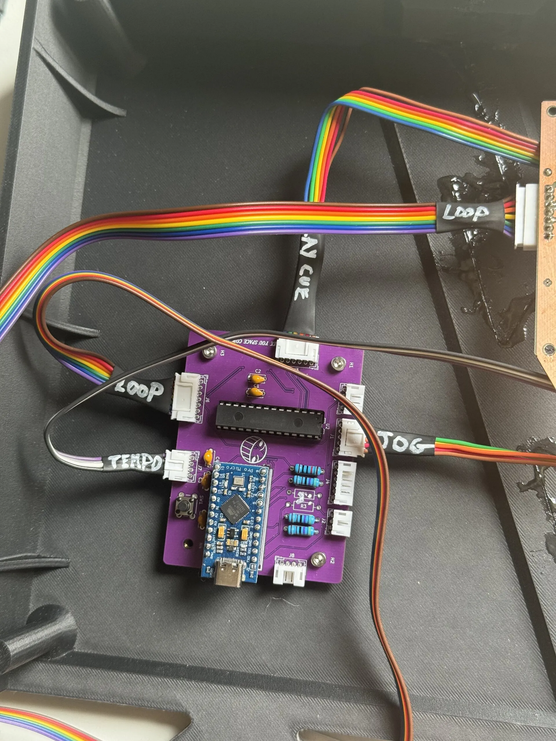 A purple board carrying a blue Arduino Pro Micro inside a black printed tray; rainbow ribbon and grey wires plug into it, tagged LOOP, TEMPO, JOG or PLAY CUE.