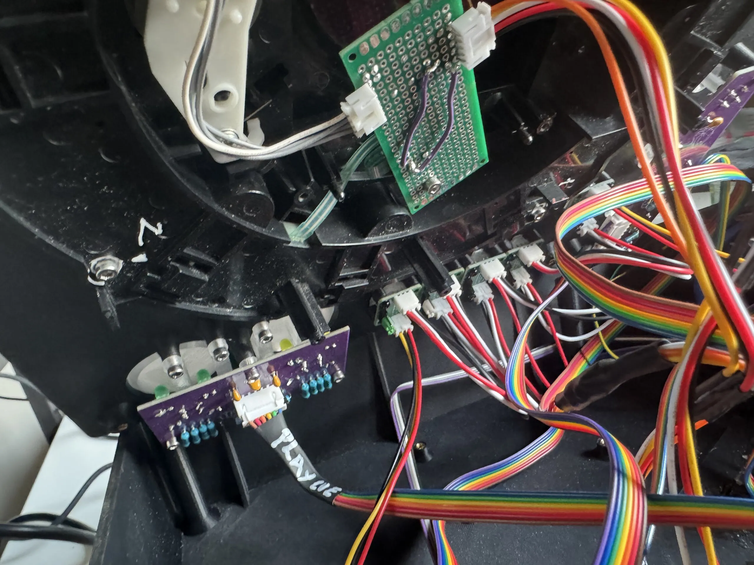 A purple board with blue resistors and a white connector whose cable is marked PLAY CUE in white pen, under two large buttons; above it, a perfboard with purple jumper wires links the jog's sensor.