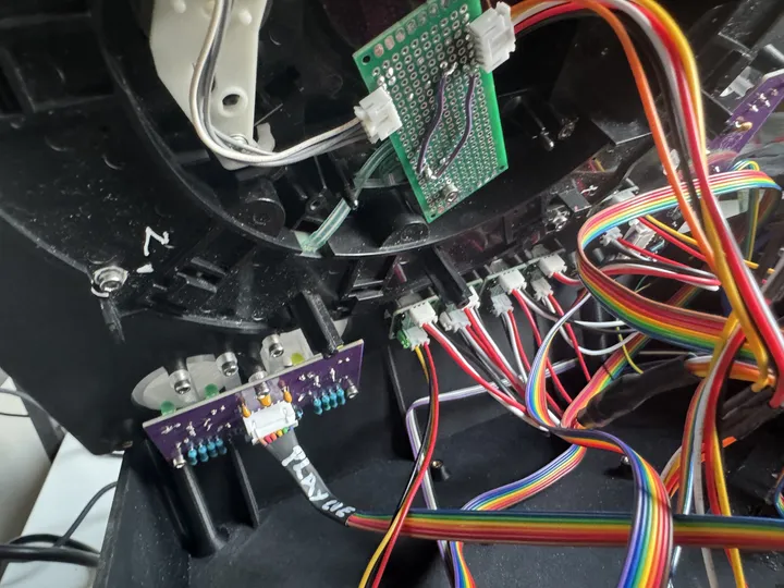 A purple board with blue resistors and a white connector whose cable is marked PLAY CUE in white pen, under two large buttons; above it, a perfboard with purple jumper wires links the jog's sensor.