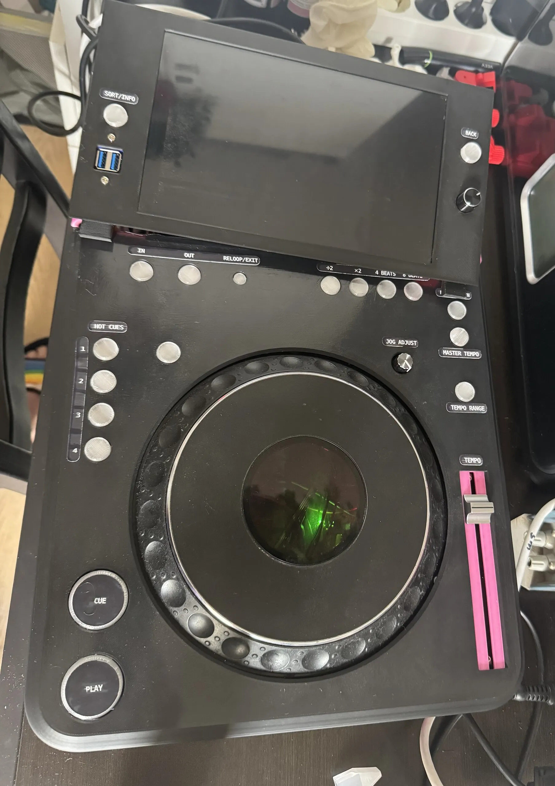 Top-down view of the deck with printed labels: SORT/INFO and BACK by the screen, IN, OUT and RELOOP/EXIT along the top, the beat-loop sizes, HOT CUES 1 to 4 down the left, JOG ADJUST, MASTER TEMPO and TEMPO RANGE on the right, a TEMPO fader in a pink slot, and CUE and PLAY at the bottom left. The screen is off.