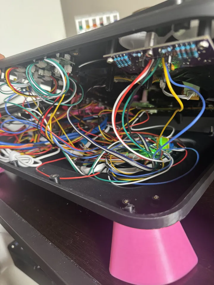 The deck's top tilted up to show its underside: a dense tangle of red, yellow, blue, green, black and white wires between purple boards and connectors, with a pink leg at the bottom.
