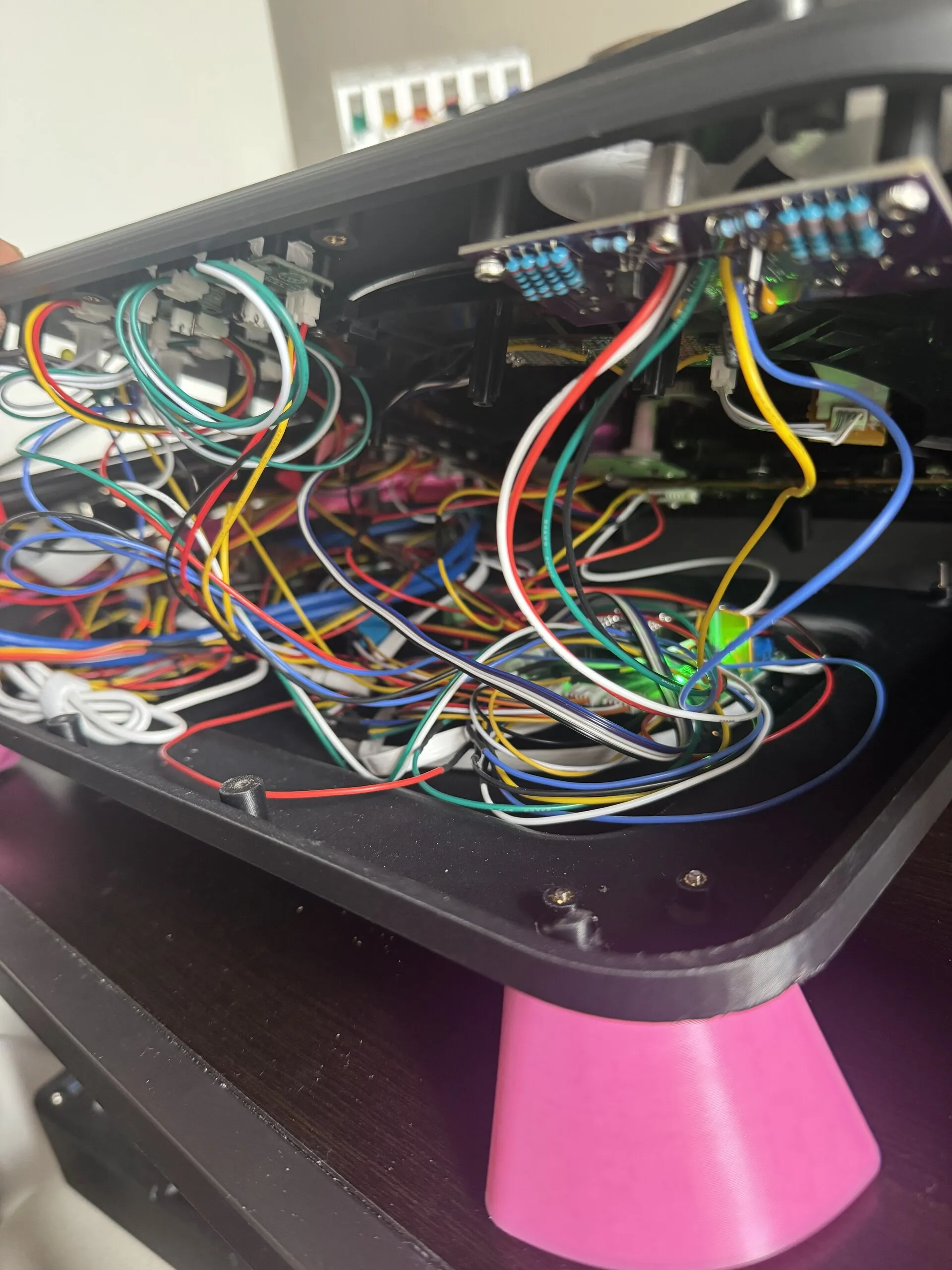 The deck's top tilted up to show its underside: a dense tangle of red, yellow, blue, green, black and white wires between purple boards and connectors, with a pink leg at the bottom.